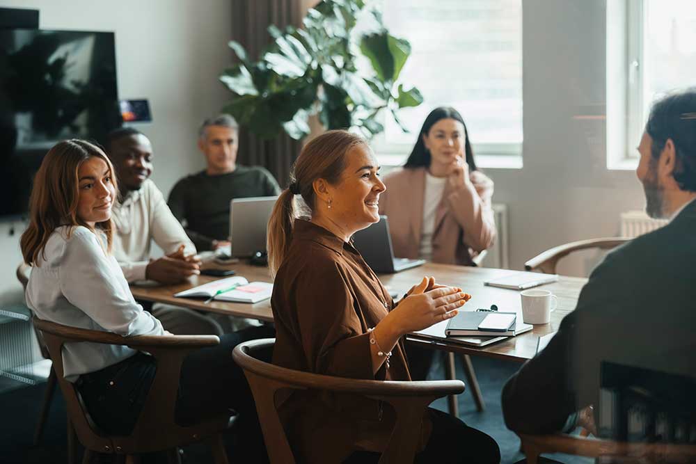 Glad affärskvinna gestikulerar och pratar med kollegor vid ett affärsmöte på modernt kontor